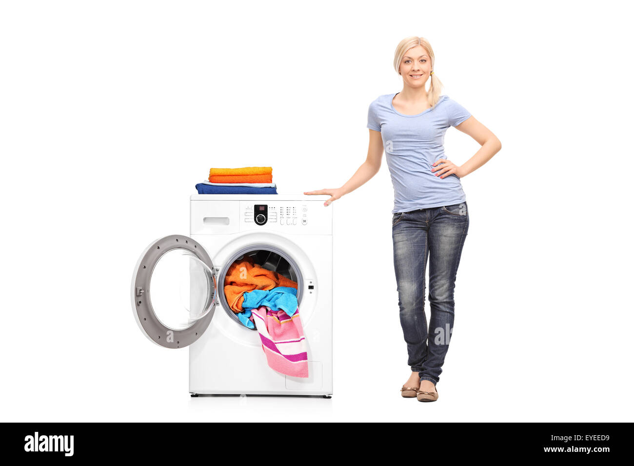 Full length portrait of a young woman standing next to a washing machine and looking at the camera isolated on white background Stock Photo