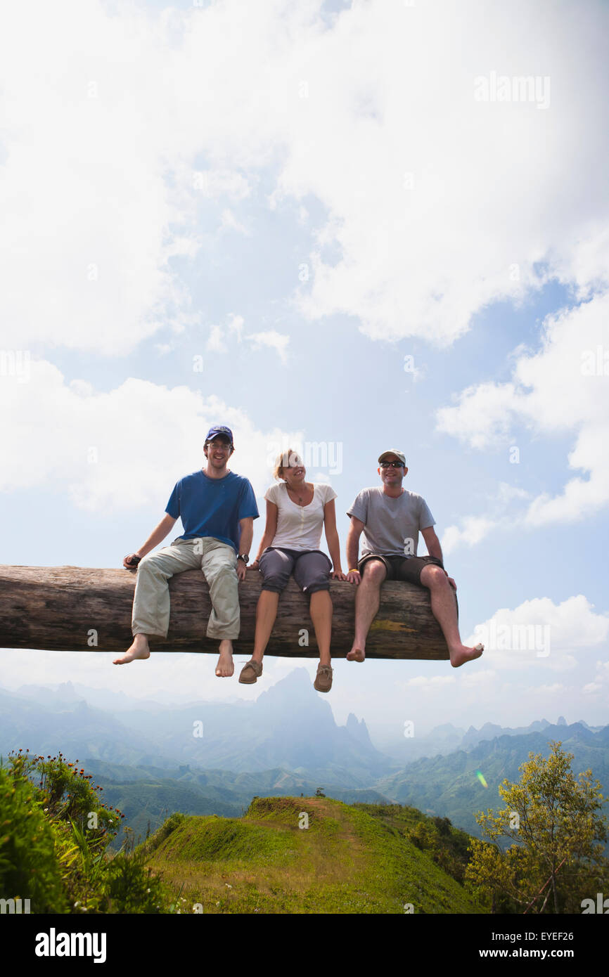 Three tourists sit on an outlook spot offering great views over the valley in Laos; Laos Stock Photo