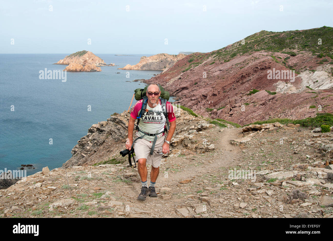 A hiker walks along a rocky northern coastal path of the Cami de Cavalls bridal trail on the island of Menorca Spain Stock Photo