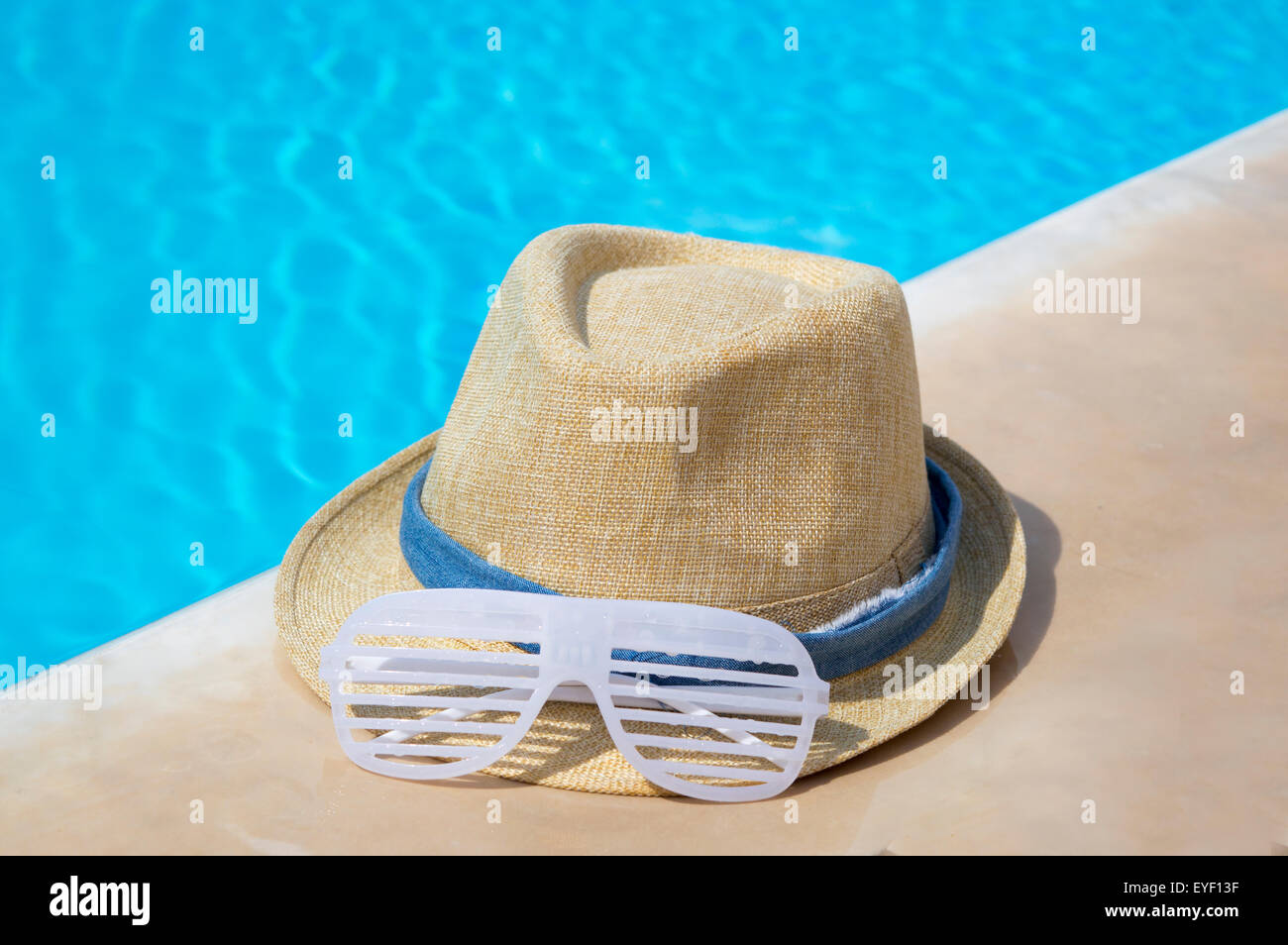 Straw hat and rave party sunglasses by the pool Stock Photo