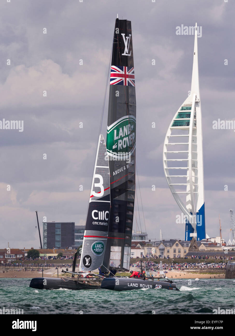 Sir Ben Ainslie's AC45 catamaran passes the Spinnaker Tower and his team HQ (large building left of the sail) during Stock Photo