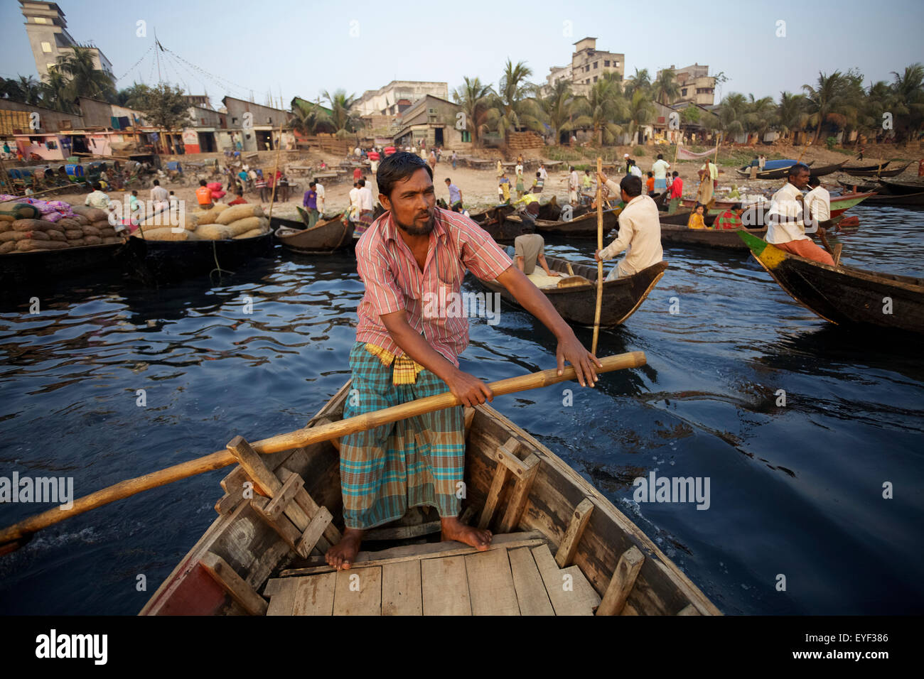 A man stands in a wooden boat rowing with large wooden paddle; Sadarghat, Dhaka, Bangladesh Stock Photo
