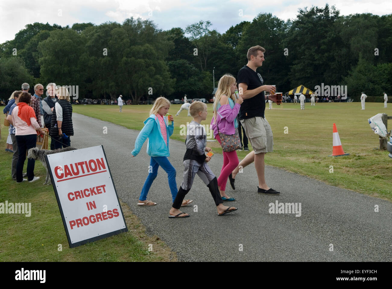 Family life in Britain, village cricket game in progress. Father and three children carrying glasses of beer group of spectators chatting.  Sussex Uk  2015 2010s HOMER SYKES Stock Photo