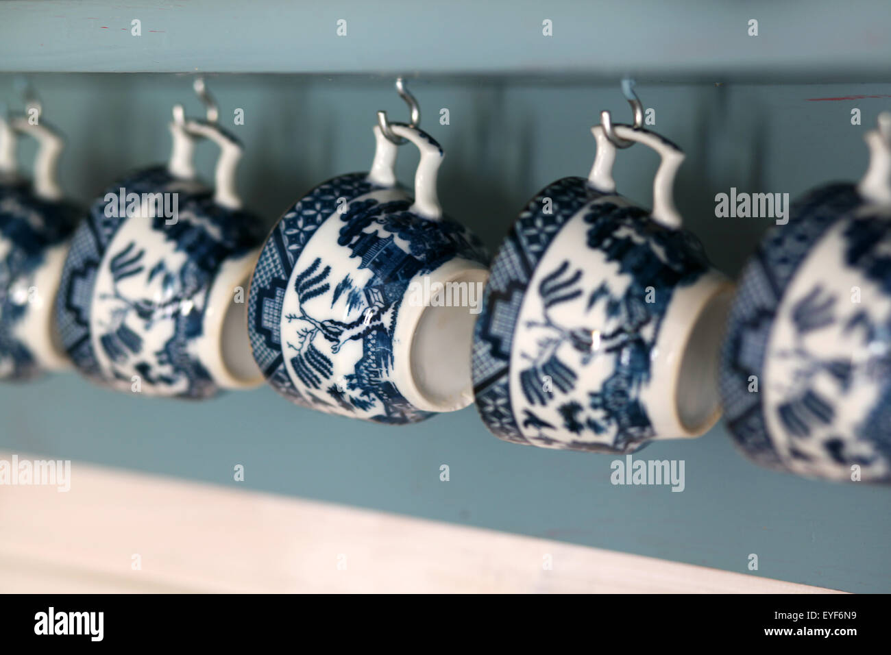 Old fashioned coffee cups hanging from lihgt blue shelf Stock Photo
