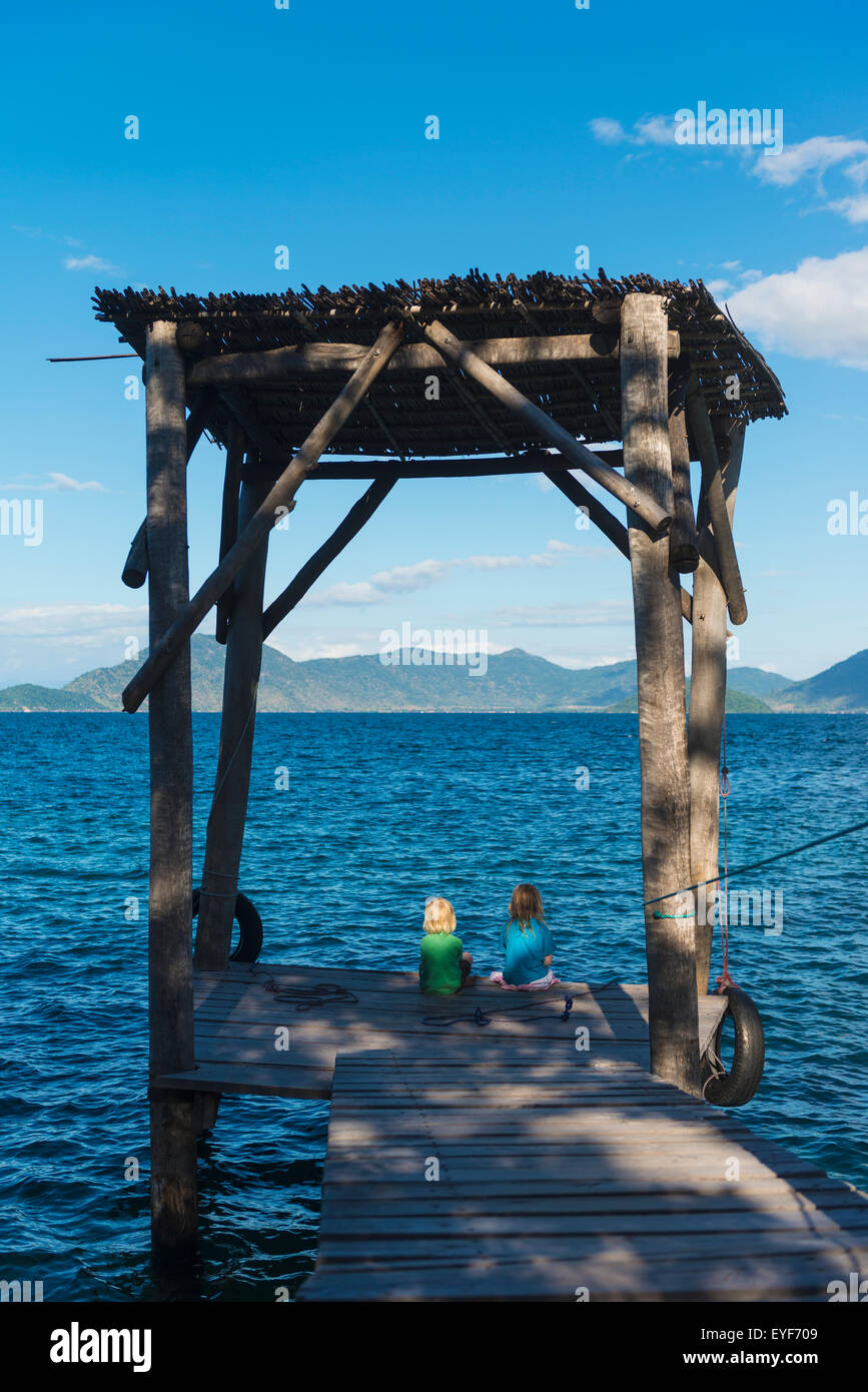 Girl and a boy sitting on the end of a jetty on Mumbo Island, Lake Malawi; Malawi Stock Photo