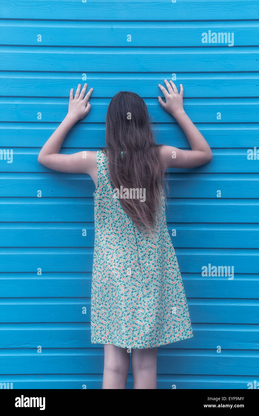 a girl with a floral dress is leaning against a wooden wall Stock Photo