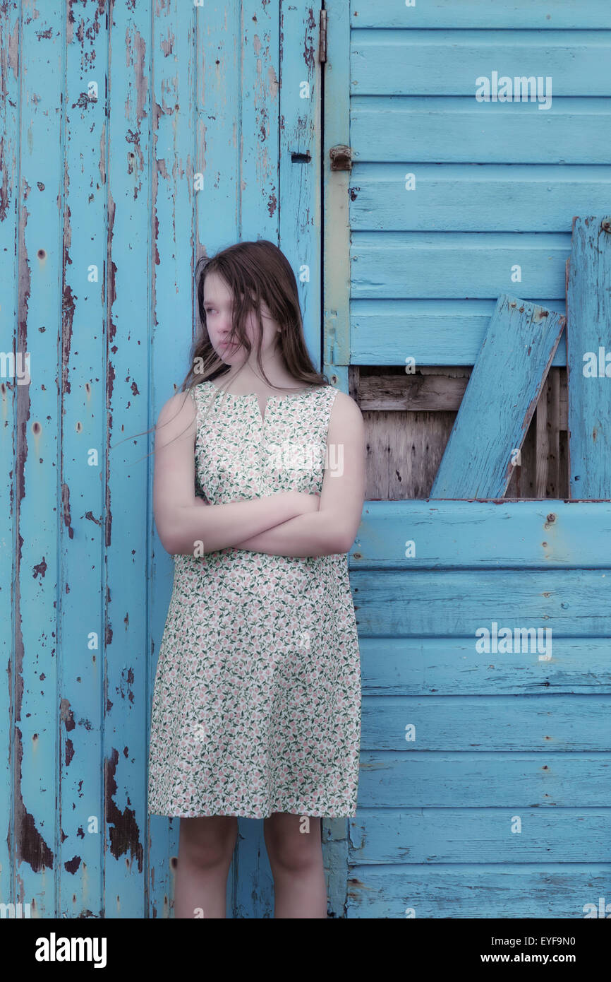 a girl in a floral dress is standing in front of a blue wooden wall ...