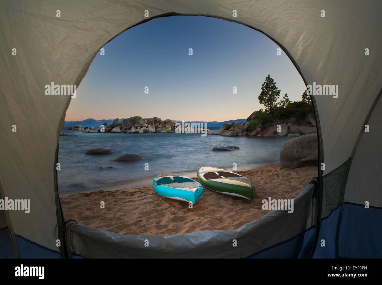 A view through a tent door of two paddle boards sitting on a beach of Lake Tahoe, California in the early evening. Stock Photo