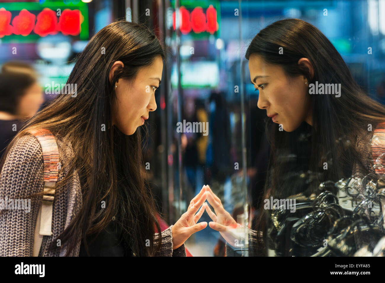 A young woman and her reflection in the glass peering into a shop window, Kowloon; Hong Kong, China Stock Photo