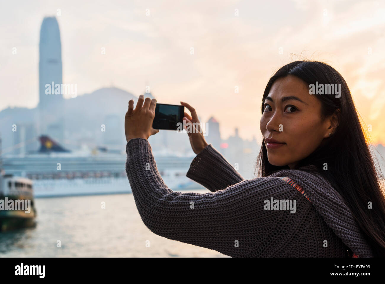 A young woman photographs buildings across the water, Kowloon; Hong Kong, China Stock Photo