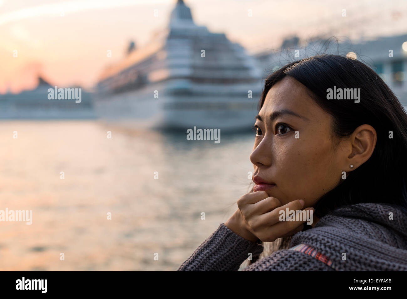 Portrait of a young woman at the waterfront with cruise ships in the harbour in the background, Kowloon; Hong Kong, China Stock Photo