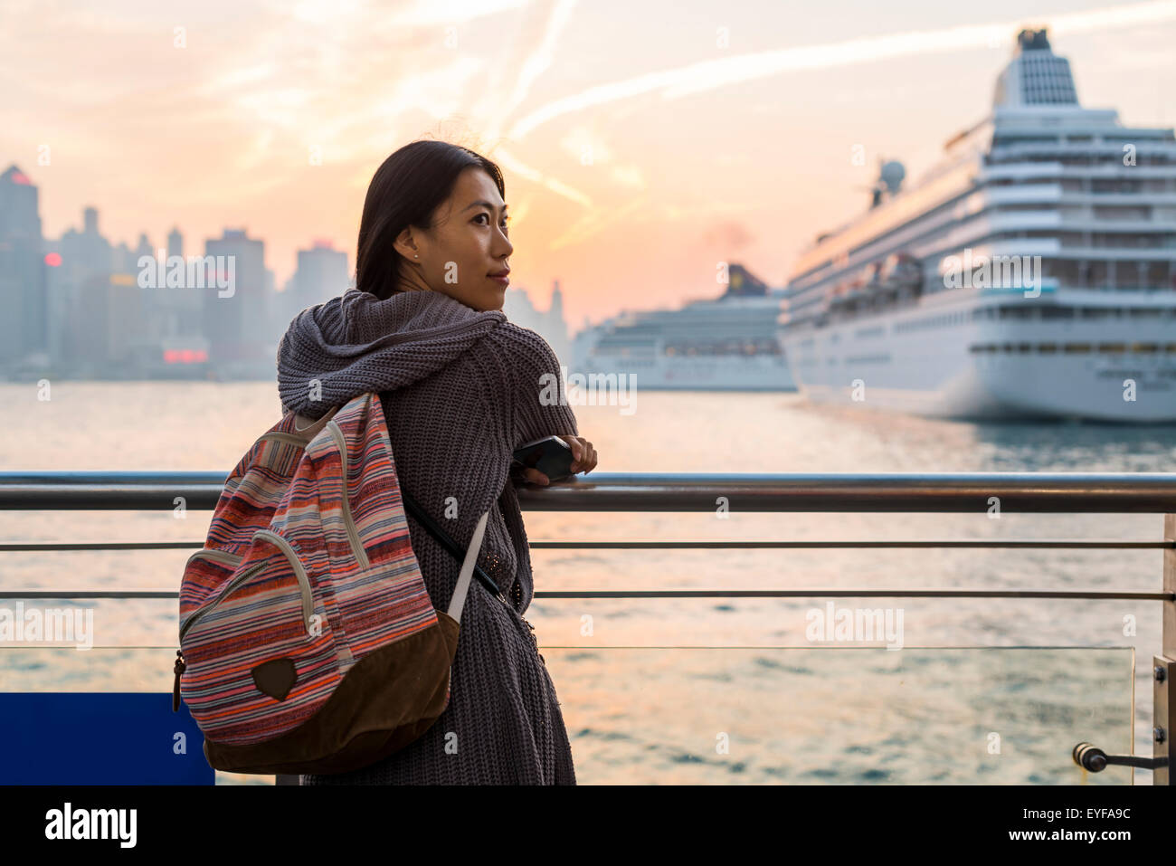 A young woman at the waterfront with cruise ships in the harbour in the background, Kowloon; Hong Kong, China Stock Photo