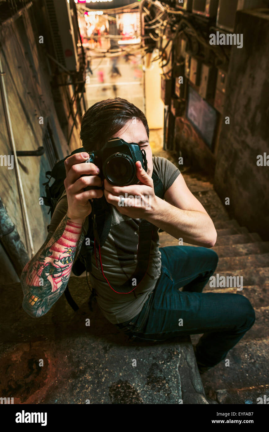 A male traveler taking a photograph with his camera in a narrow street; Xiamen, Fujian, China Stock Photo
