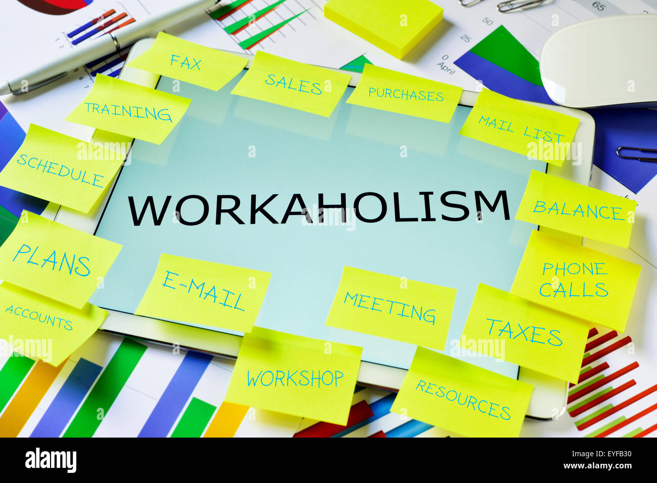 the text workaholism in a tablet computer full of sticky notes with different tasks,  placed on an office desk full of charts Stock Photo