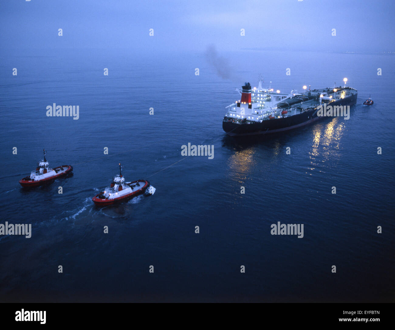 oil tanker with three tug boat assists pre-dawn aerial Stock Photo