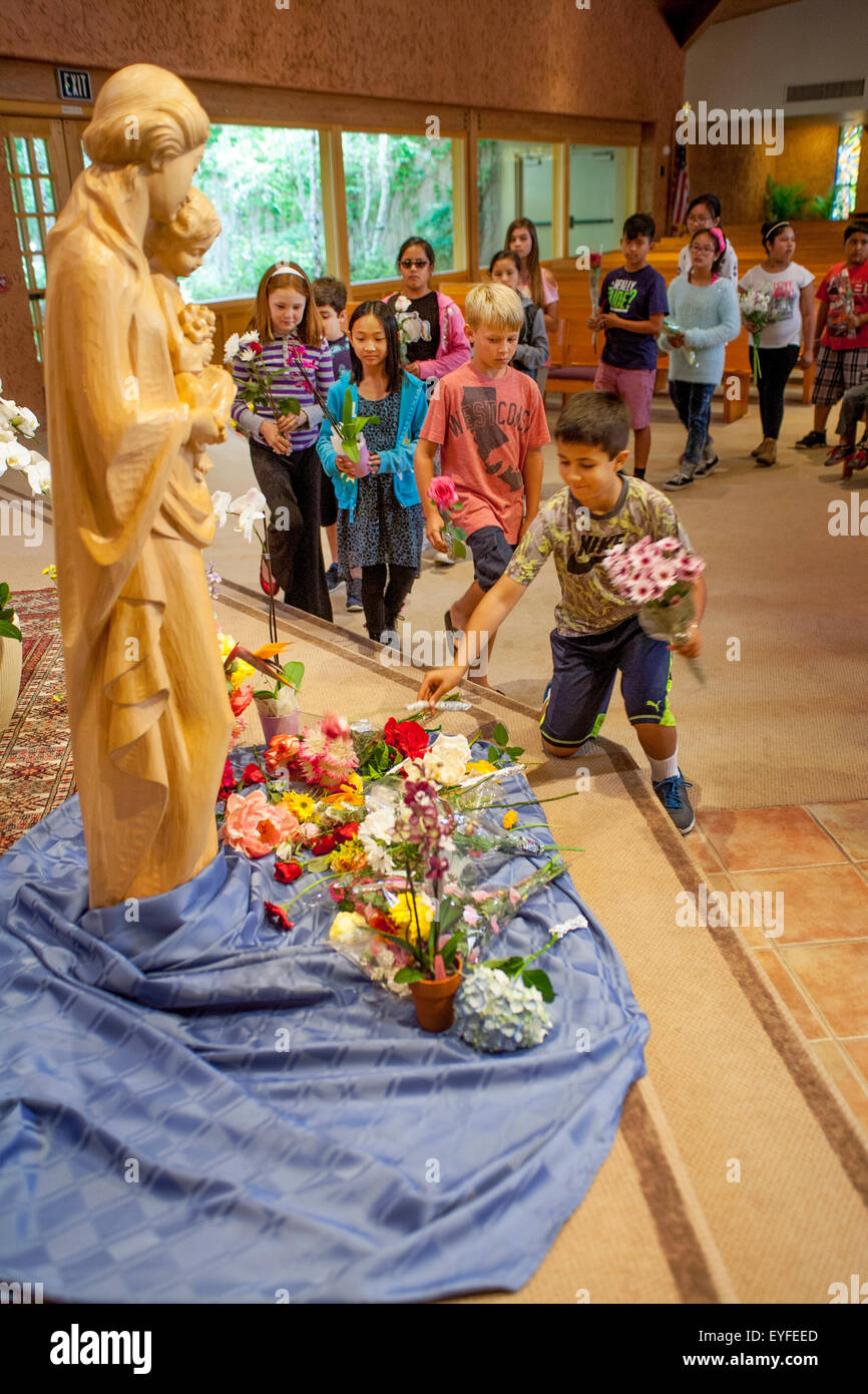 A gold statue of the Virgin Mary is decorated by bouquets brought by multiracial children at the Crowning of Mary at a Laguna Niguel, CA, Catholic church. May Devotions to the Blessed Virgin Mary are a traditional Roman Catholic ritual honoring her as 'the Queen of May.' Stock Photo