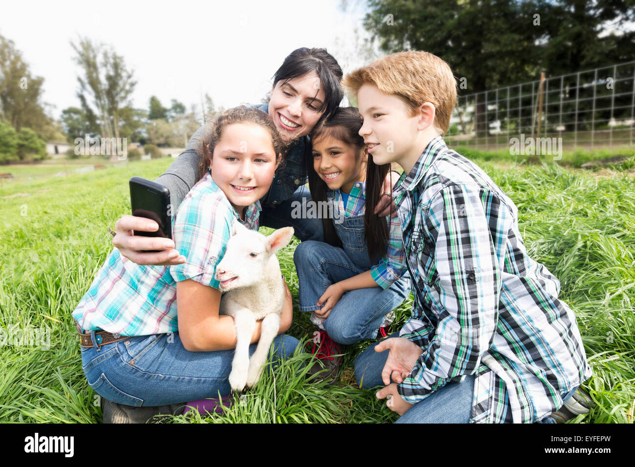 Woman with girls(6-7, 12-13) and boy (10-11) photographing with lamb Stock Photo