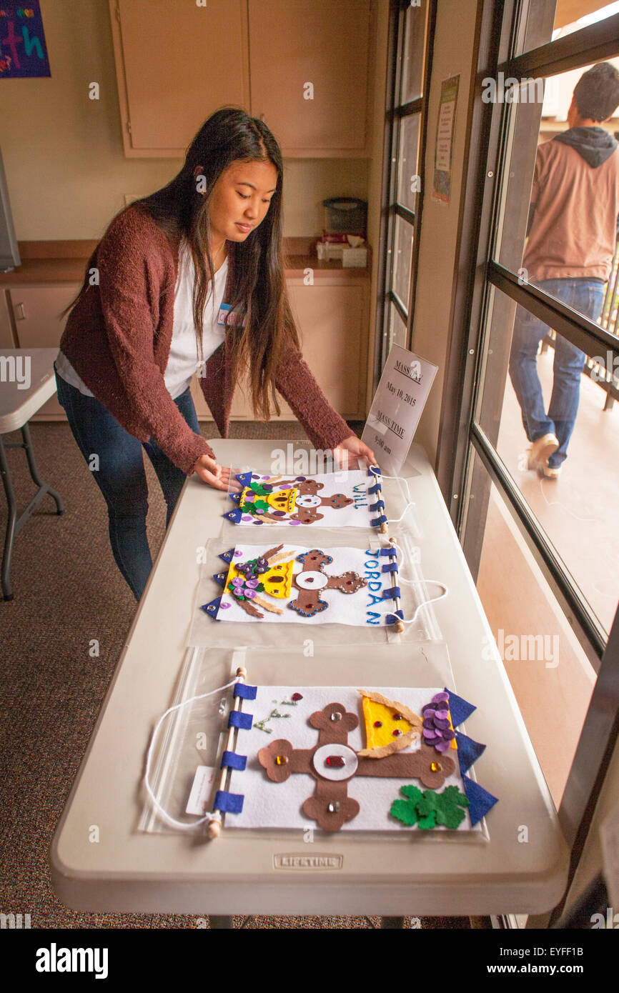 A teen Asian volunteer at a Laguna Niguel, CA, Catholic church displays newly made First Holy Eucharist banners to be used as pew markers for First Communion ceremonies. Stock Photo