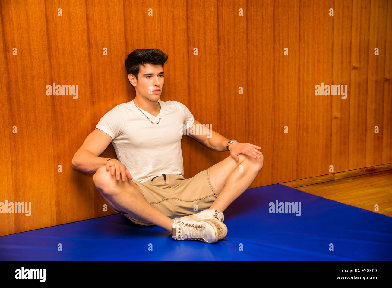 Attractive young man stretching on gym mat, pressing on knees to open legs Stock Photo
