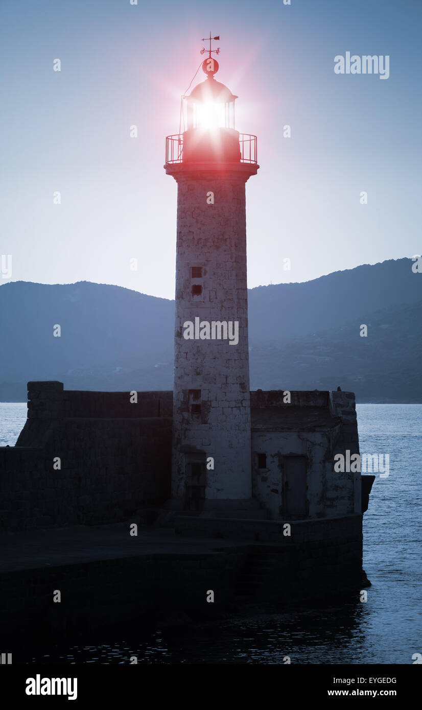 Old lighthouse tower silhouette on the coast of Mediterranean Sea, red light. Blue toned, stylized night photo Stock Photo