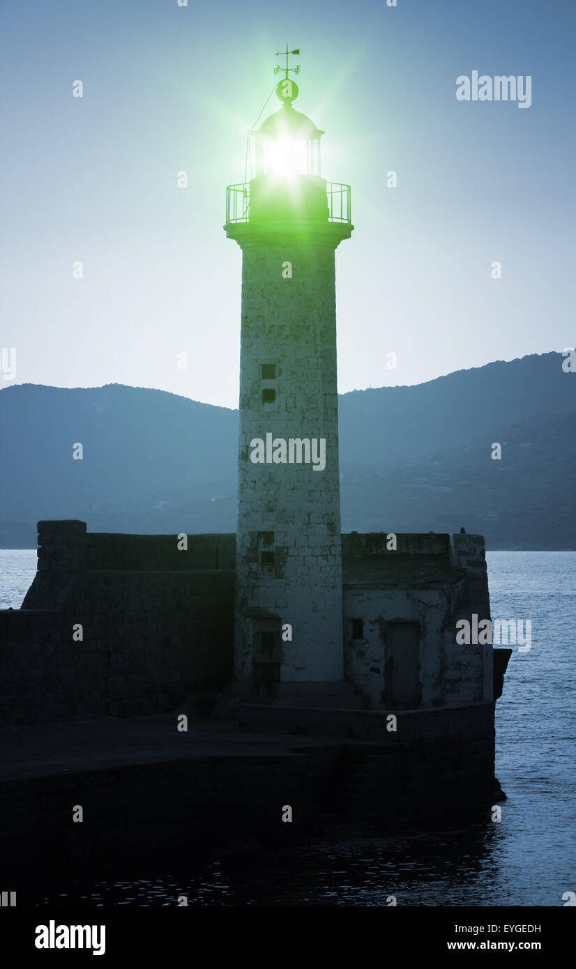 Old lighthouse tower silhouette on the coast of Mediterranean Sea, green light. Blue toned, stylized night photo Stock Photo