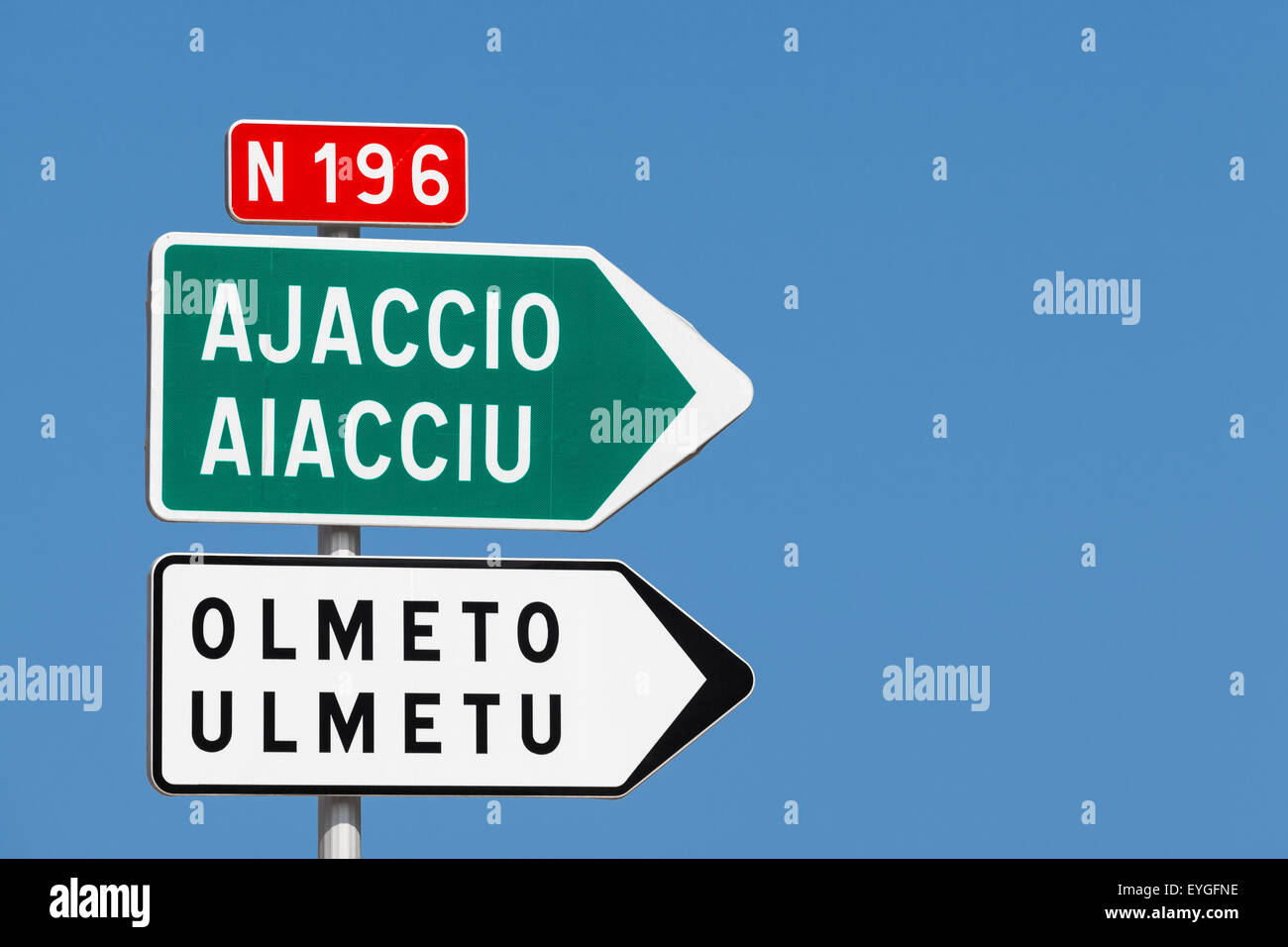 Road sign. White and green arrows with destination cities names and red road number label over clear blue sky background Stock Photo