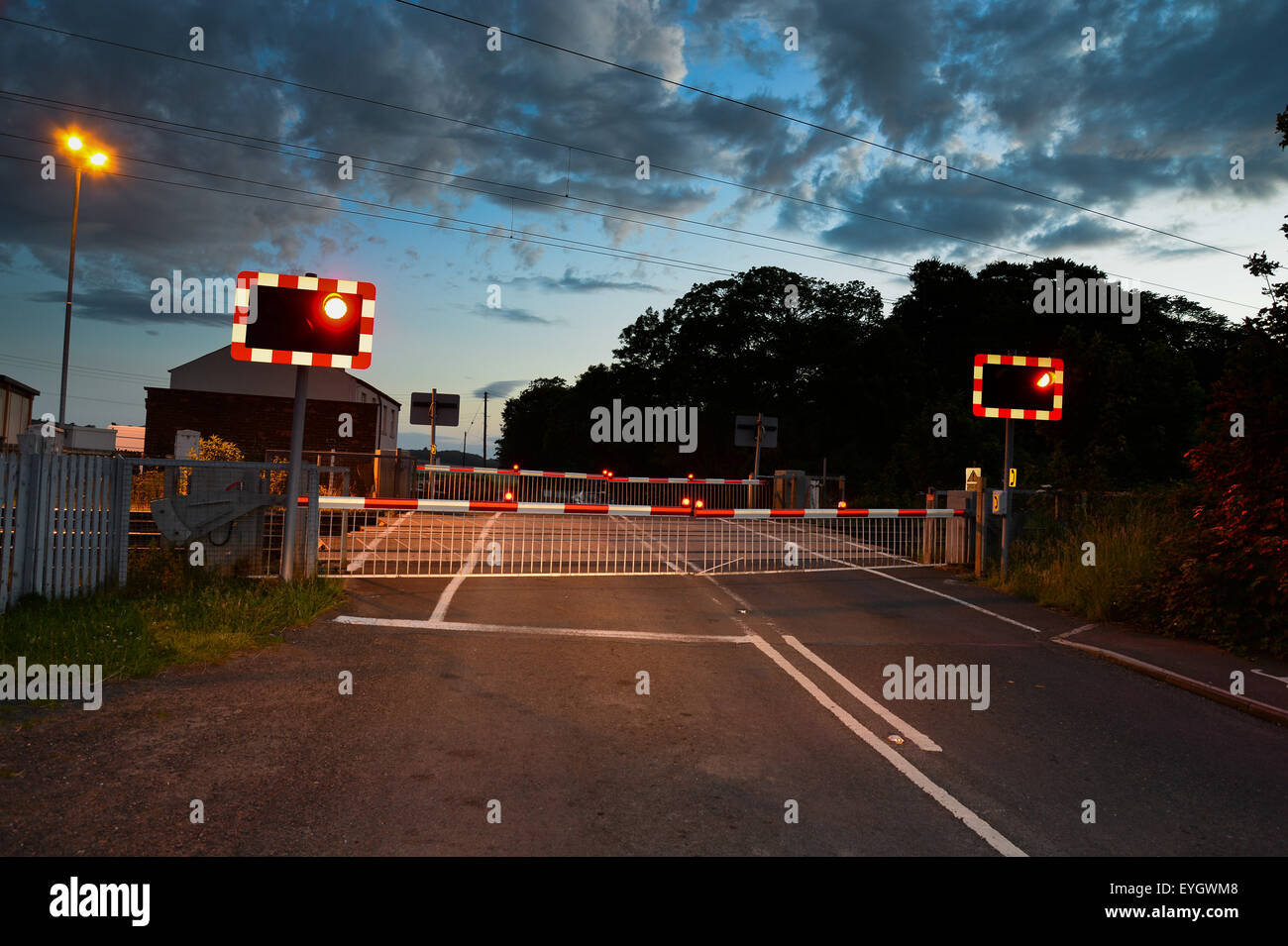 A railway level crossing at night with the barriers down and the lights at red. Stock Photo