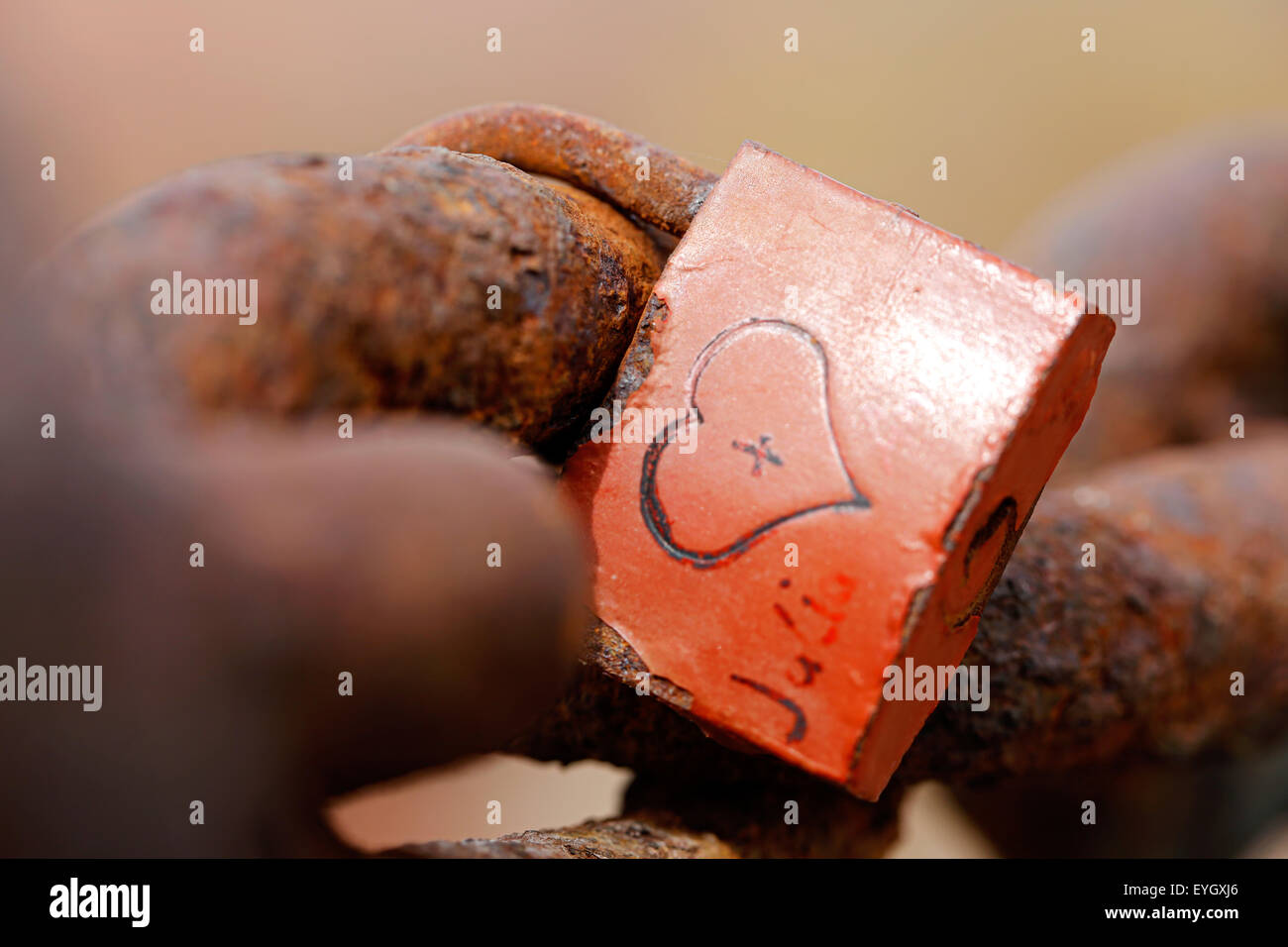 An old weathered love lock attached to a rusty old chain. the lock has a heart shape carved into its body and initials on either side of the heart Stock Photo