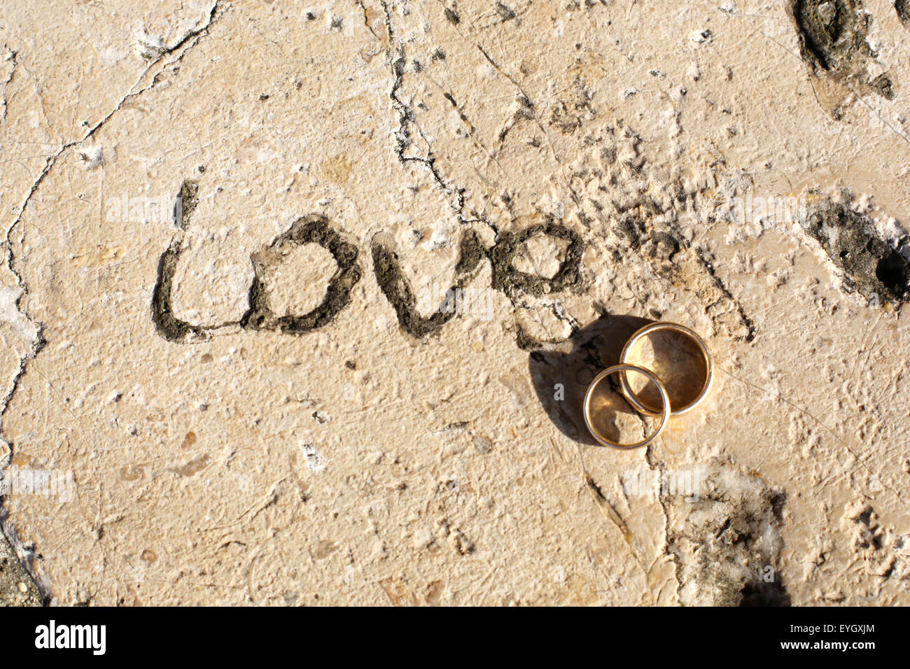 Two gold wedding rings, inter twined beside the word 'Love' carved into an old stone seat outside a church Stock Photo