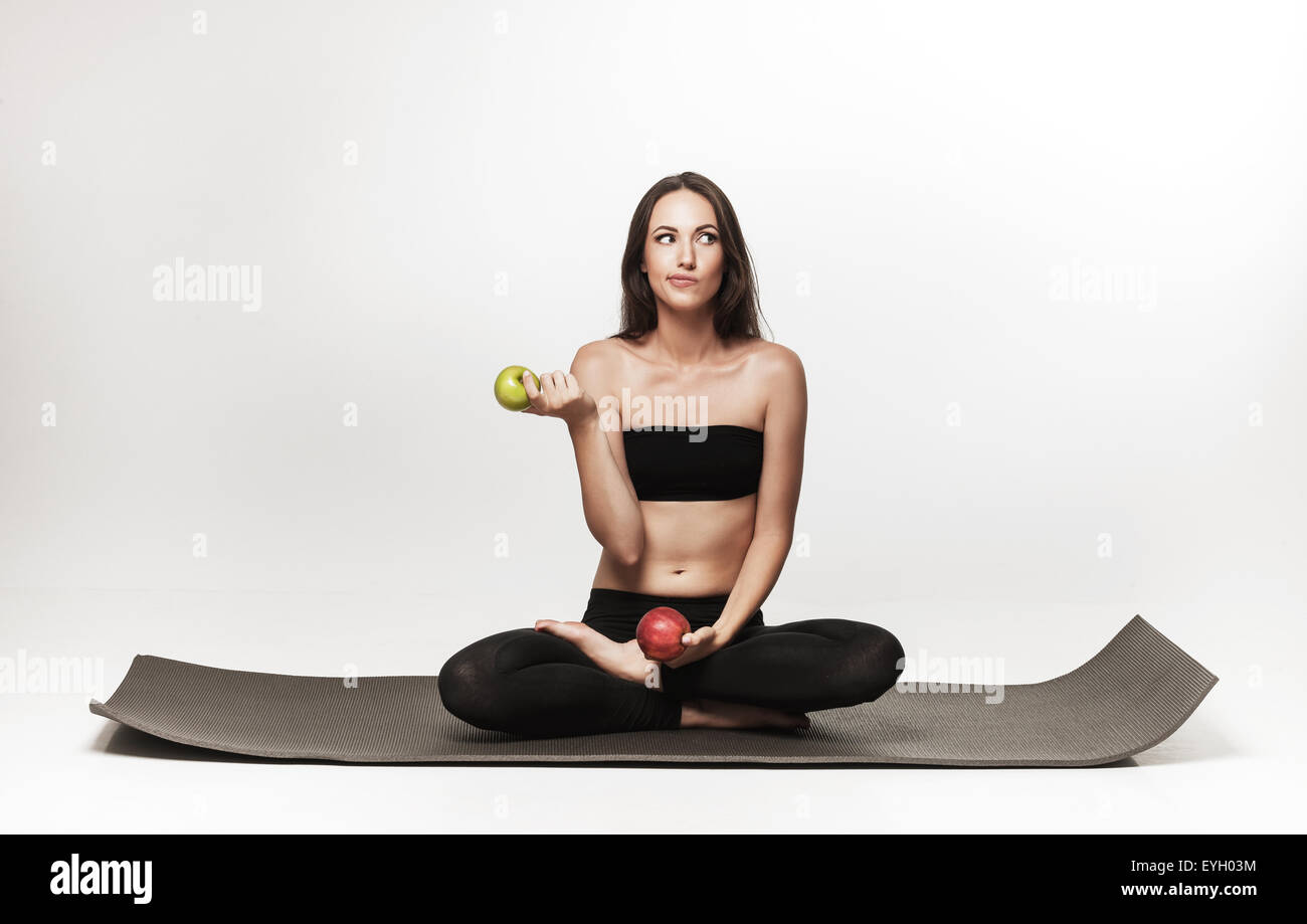 Young woman sitting on yoga mat. Woman holding apple. Healthy