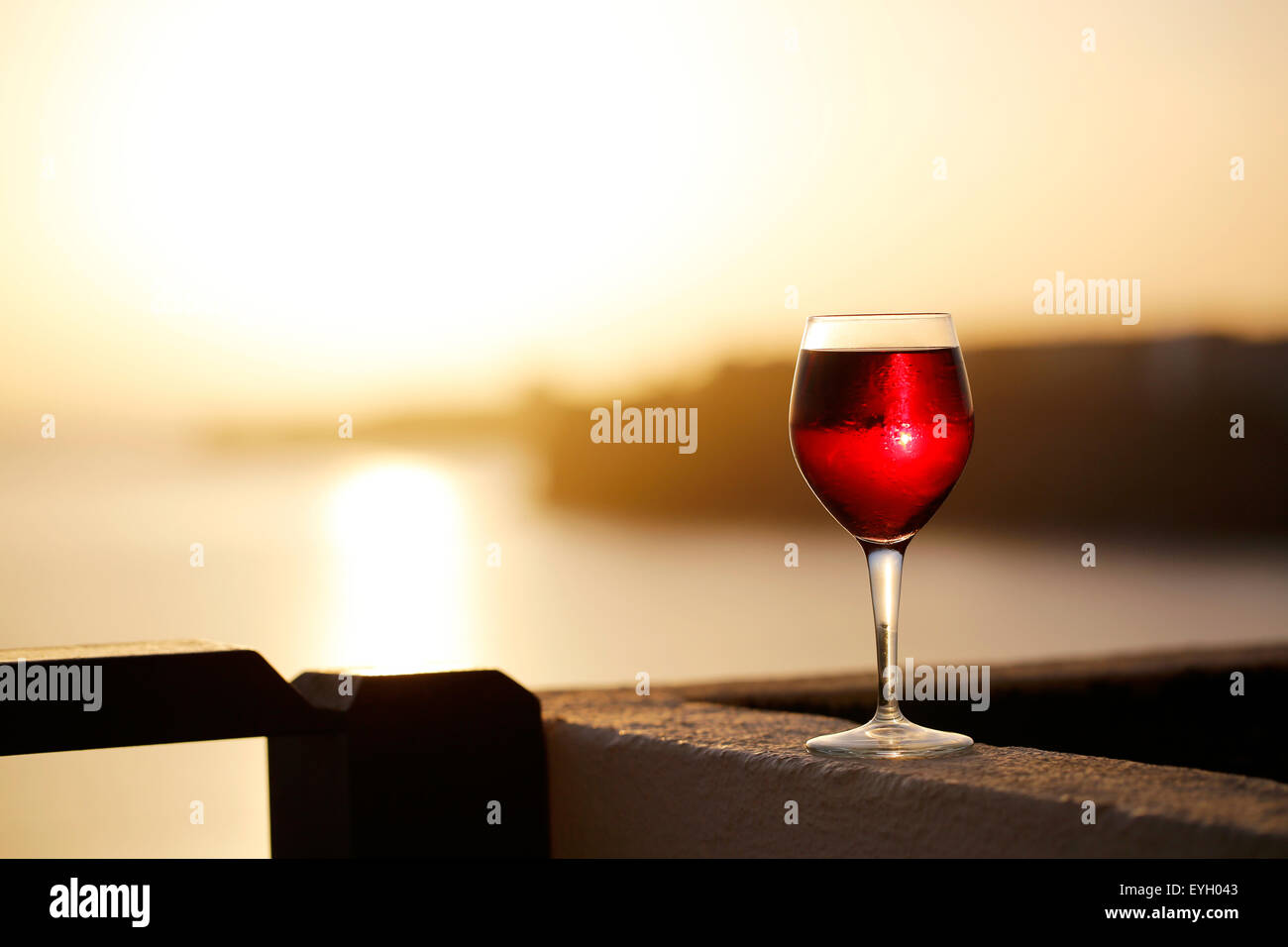 A glass of red wine on a balcony at dusk with a sunset in the background. taken in a holiday resort in Lanzarote Spain. Stock Photo