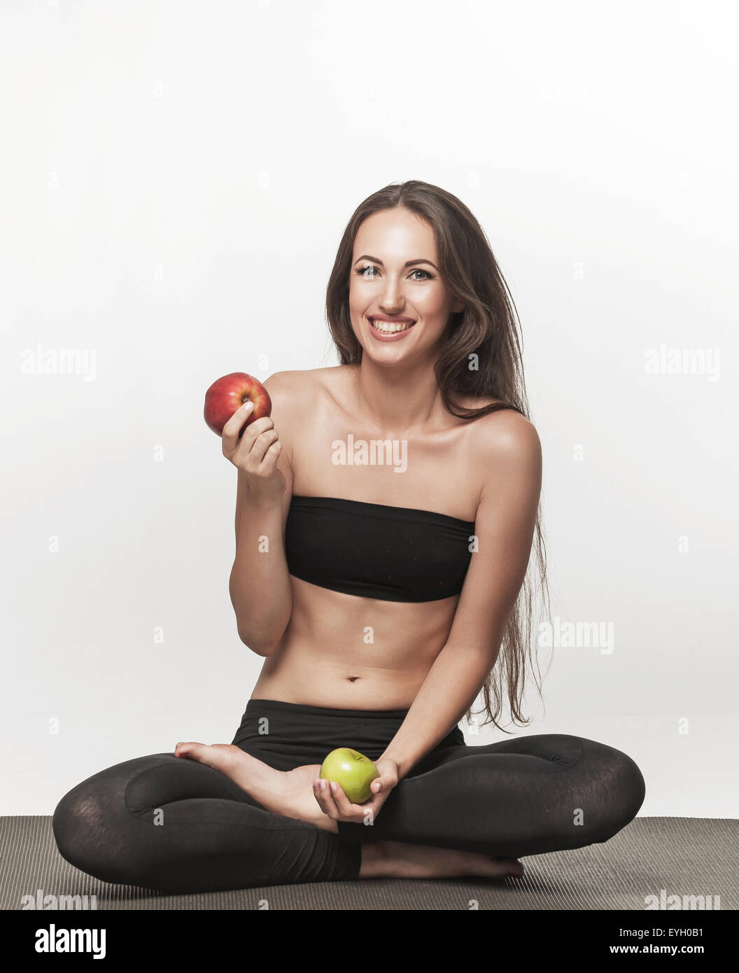 Young woman sitting on yoga mat. Woman holding apple. Healthy