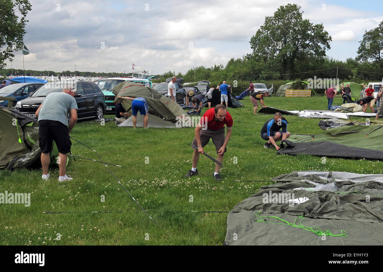 Random people on camp site struggling putting up tents in a field Stock Photo