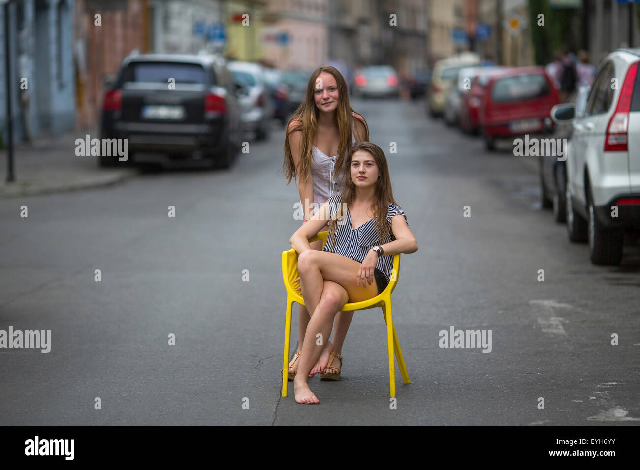 Cute adolescent girls sitting on a chair in the middle of the streets of the old town. Stock Photo