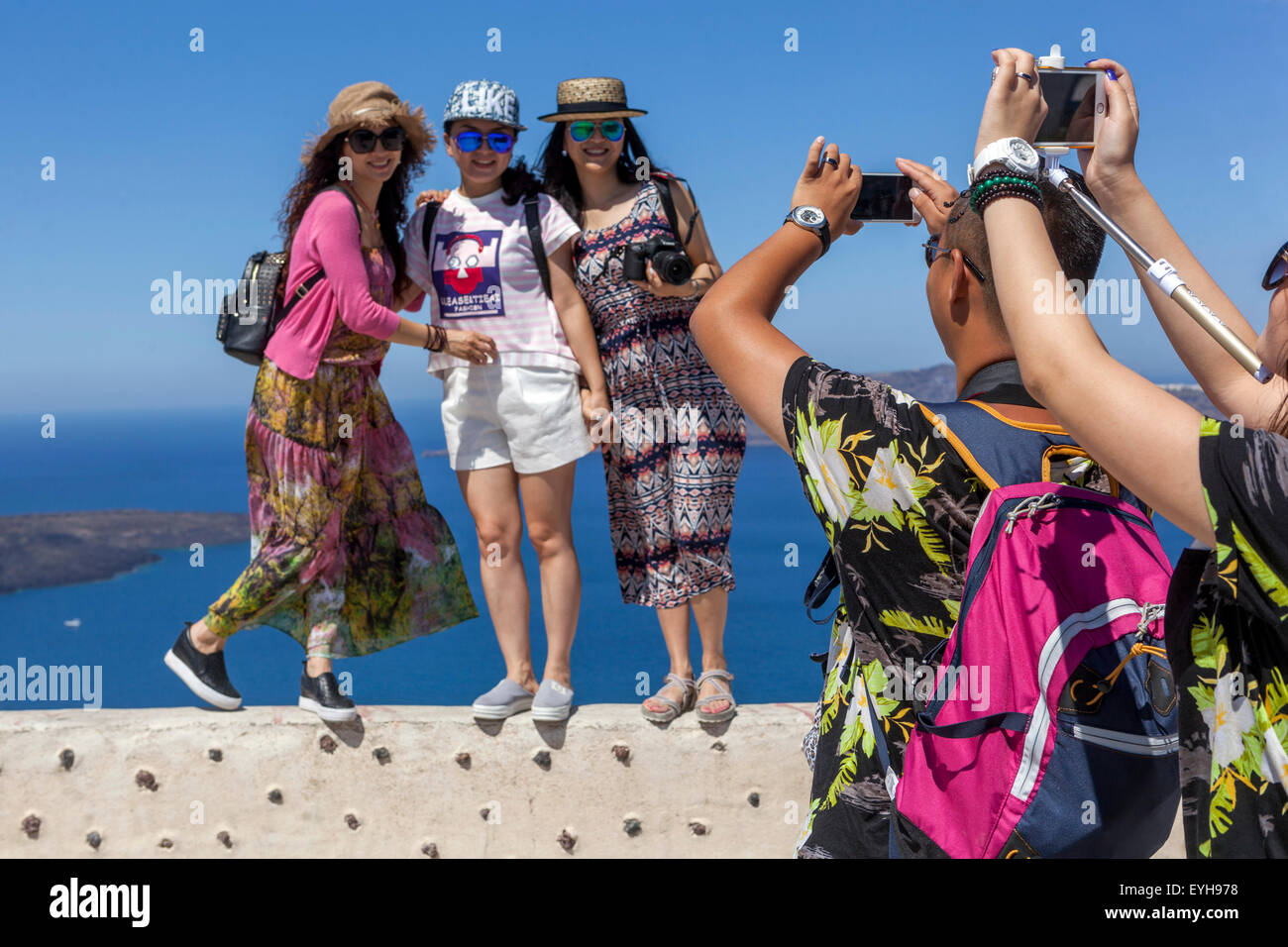 Asian tourists Europe, Young Chinese people taking photos on mobile, phone in the village of Firostefani, over the caldera. Santorini, Greece Europe Stock Photo