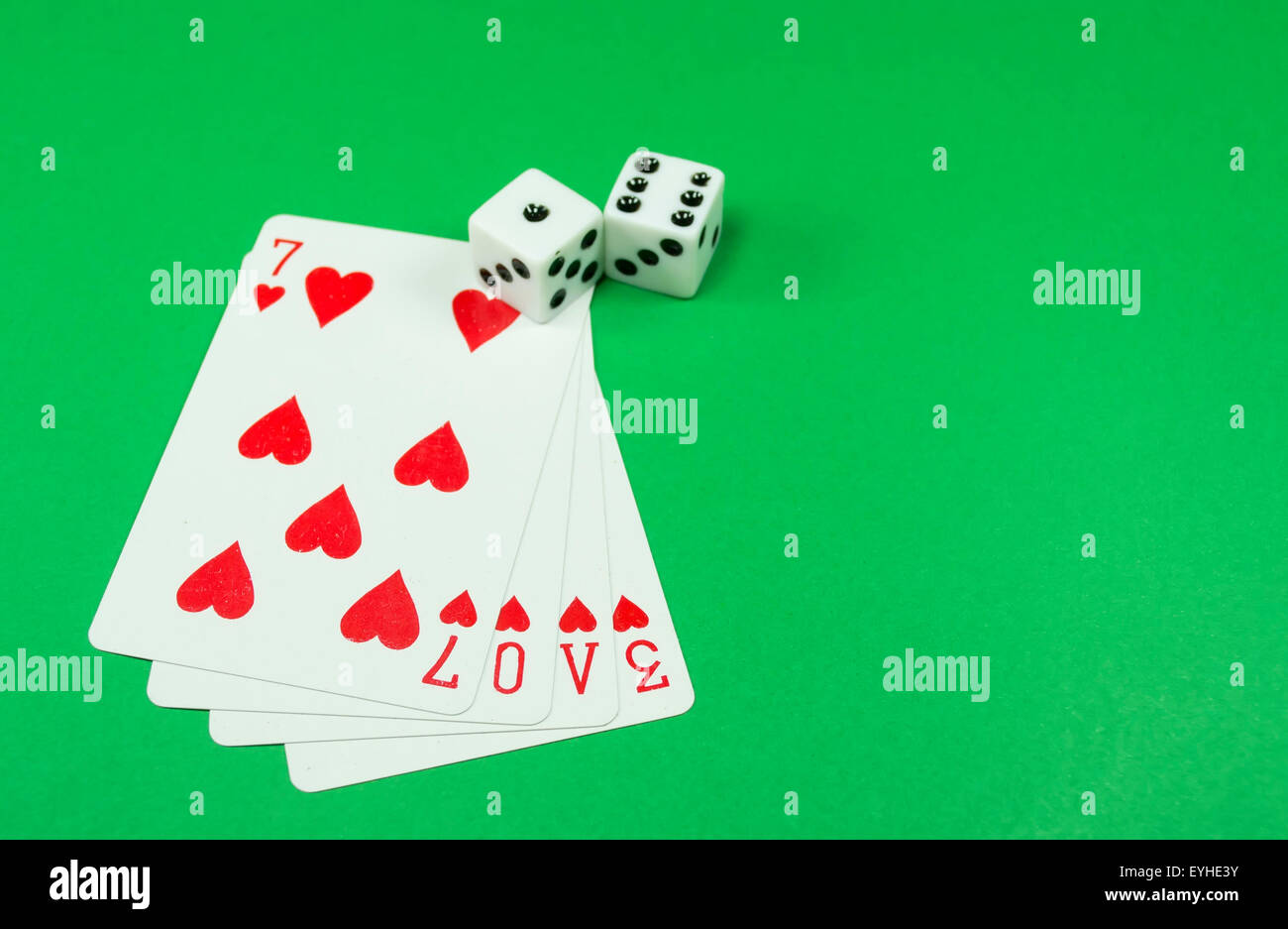 Four hearts playing cards forming the word love and tow dice against a green background, conceptual image about love Stock Photo