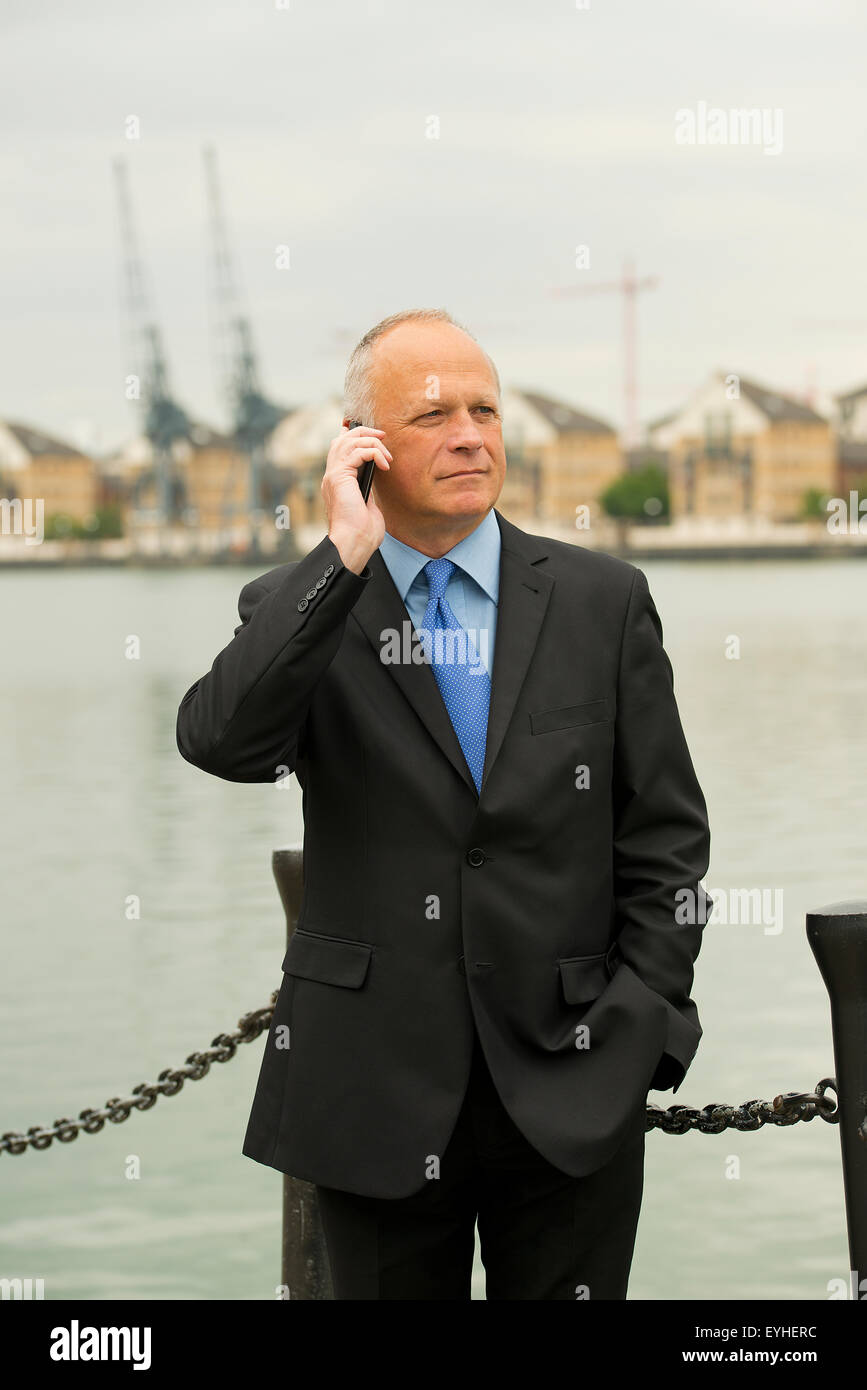 Businessman wearing a dark suit, talking on his mobile phone and situated at London's Docklands. Stock Photo