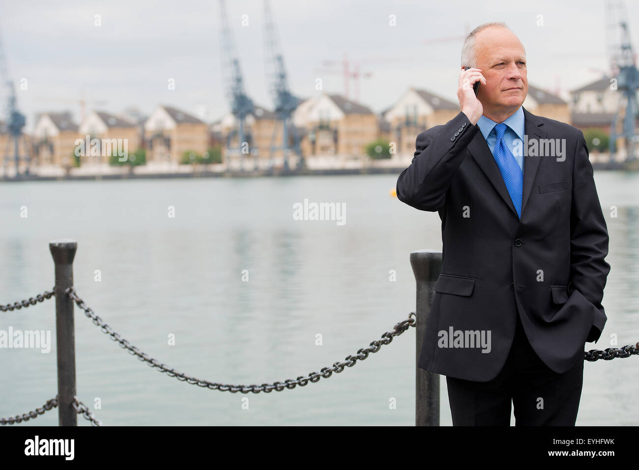 Businessman wearing a dark suit, talking on his mobile phone and situated at London's Docklands. Stock Photo