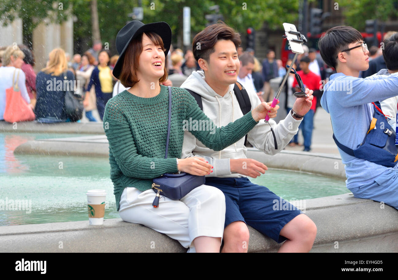 London, England, UK. Young Japanese couple in Trafalgar Square taking their photo with a selfie stick Stock Photo