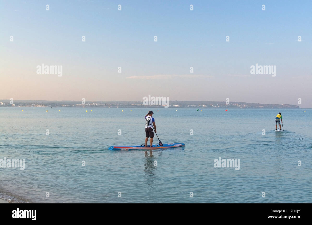 Two paddle board surfers depart in blue calm water at dawn in Can
