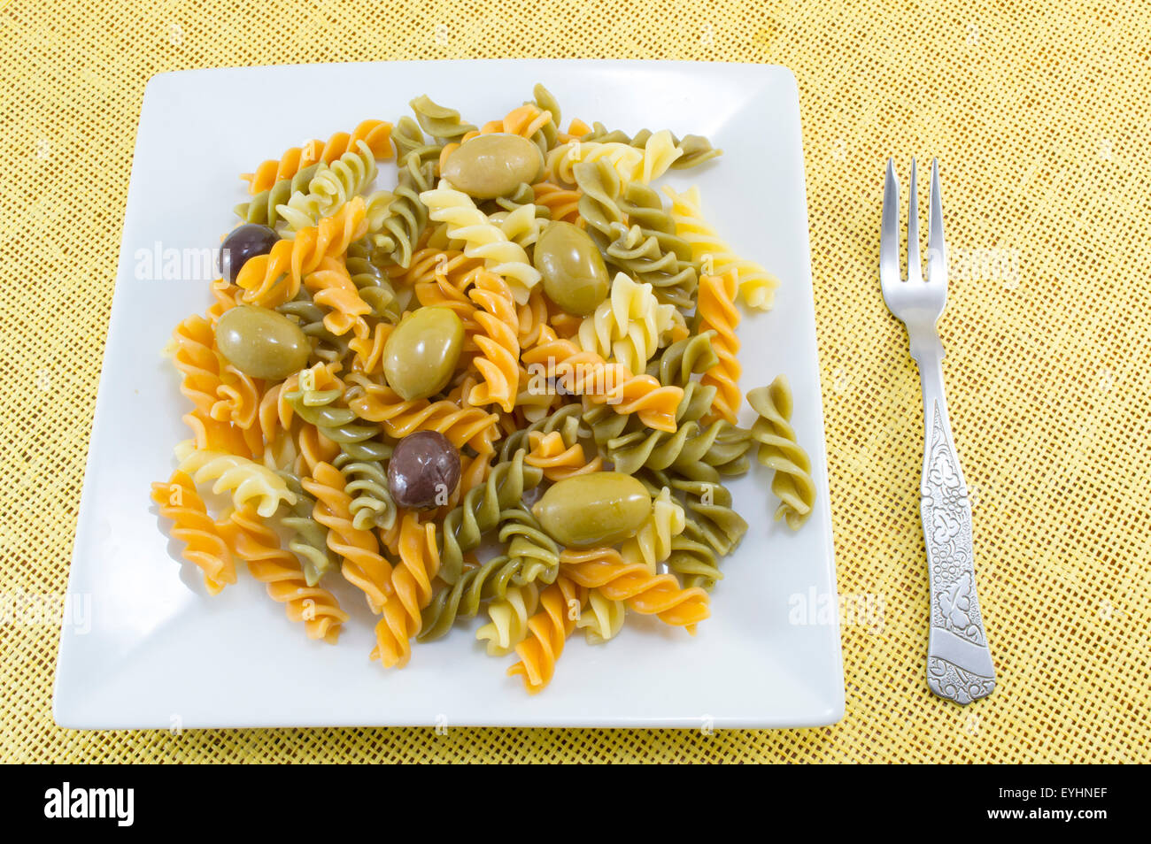 Colored macaroni pasta meal  with olives served on the yellow tablecloth with a fork Stock Photo