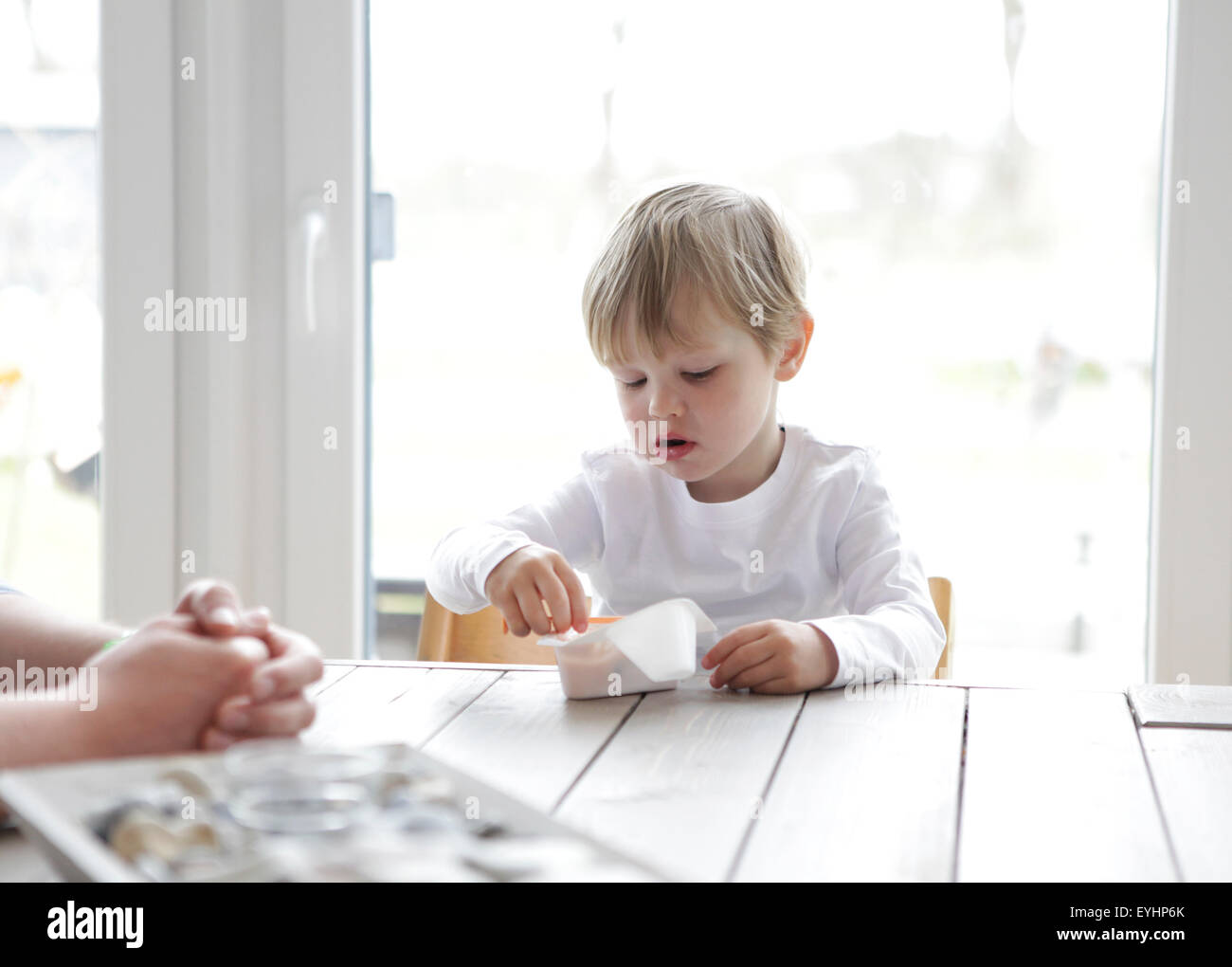 a little boy sitting at the kitchen table, eating yogurt with a spoon Stock Photo