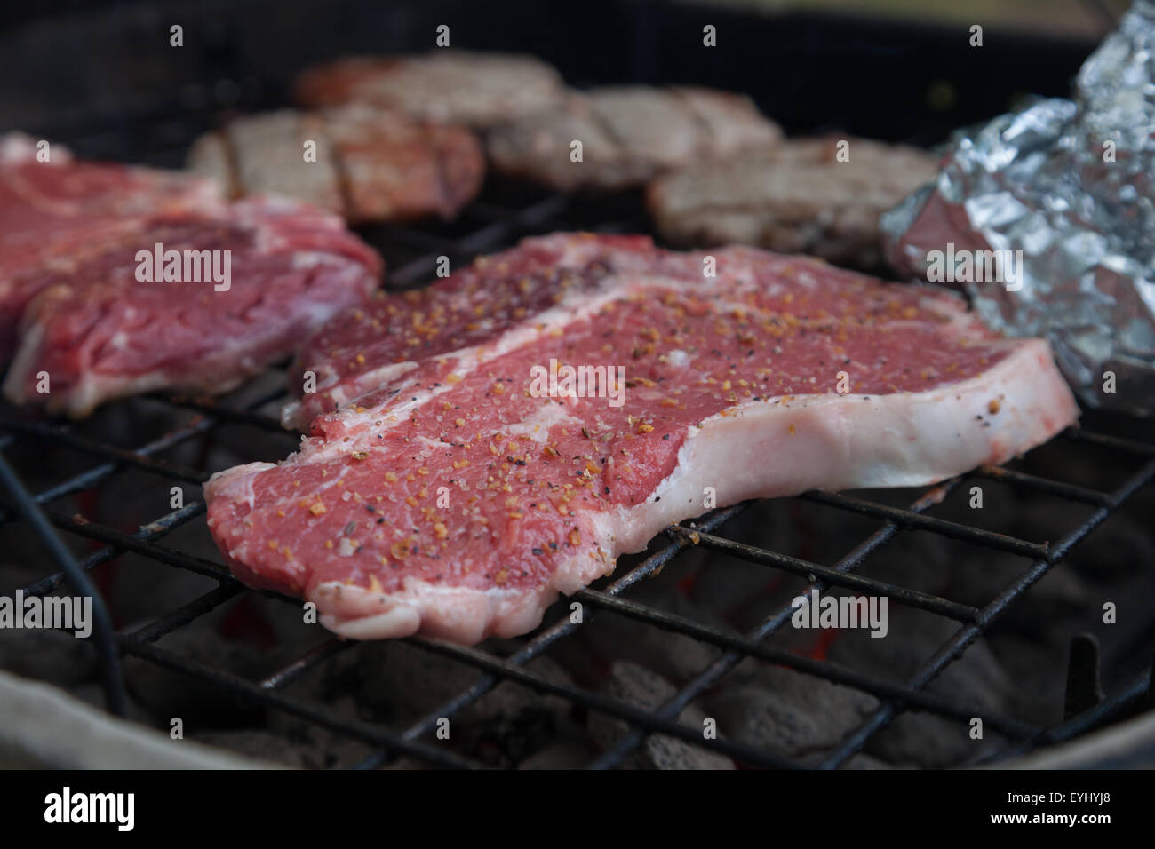 Tbone steaks sit sooking with other foods on a charcoal grill Stock