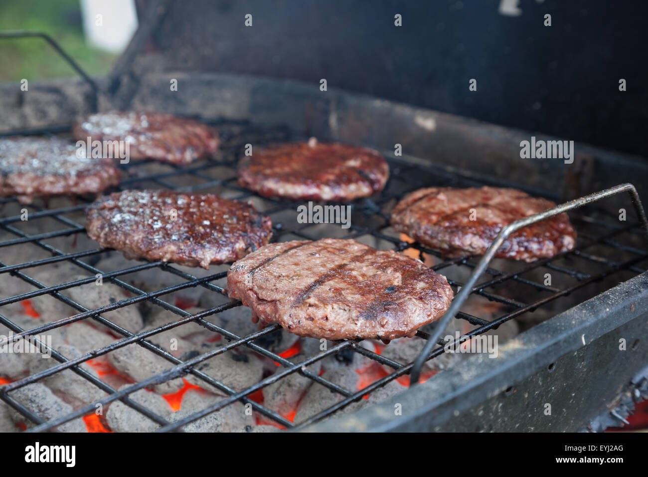 Hamburgers sit grilling on a smoky grill Stock Photo