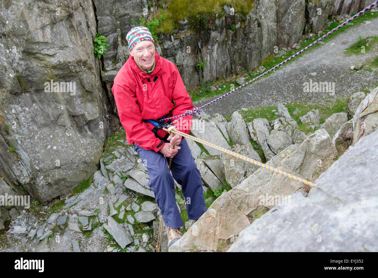 Happy active senior man having fun abseiling with a safety rope on a steep rockface for wellbeing outdoors. North Wales, UK, Britain Stock Photo