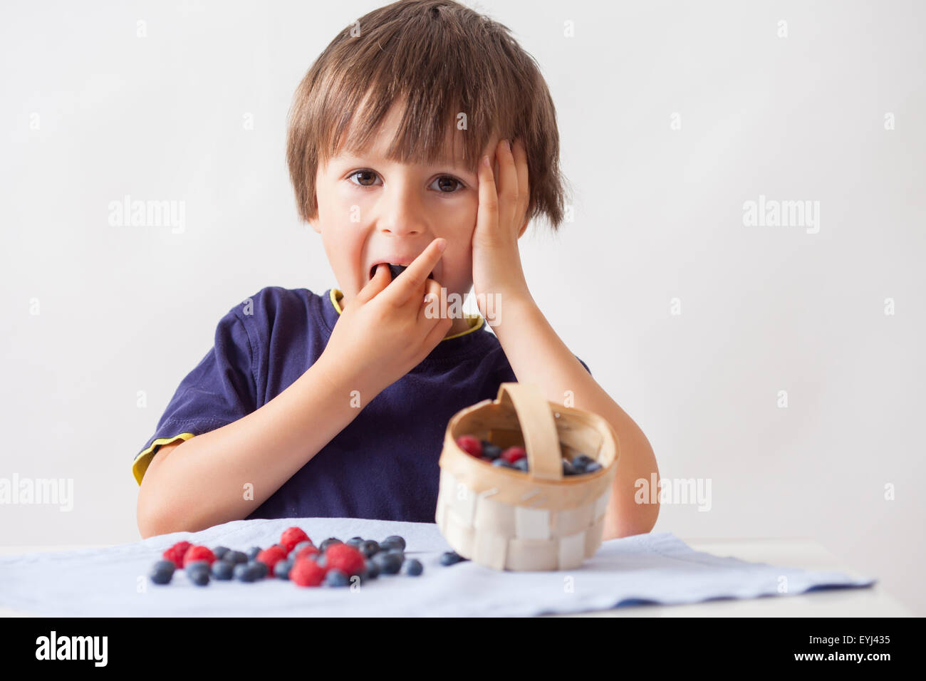 Child, sitting behind a table with raspberries and blueberries, eating ...