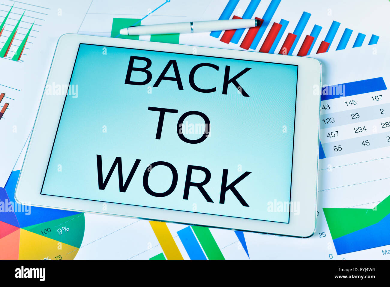 the text back to work in a tablet computer, placed on an office desk full of charts Stock Photo