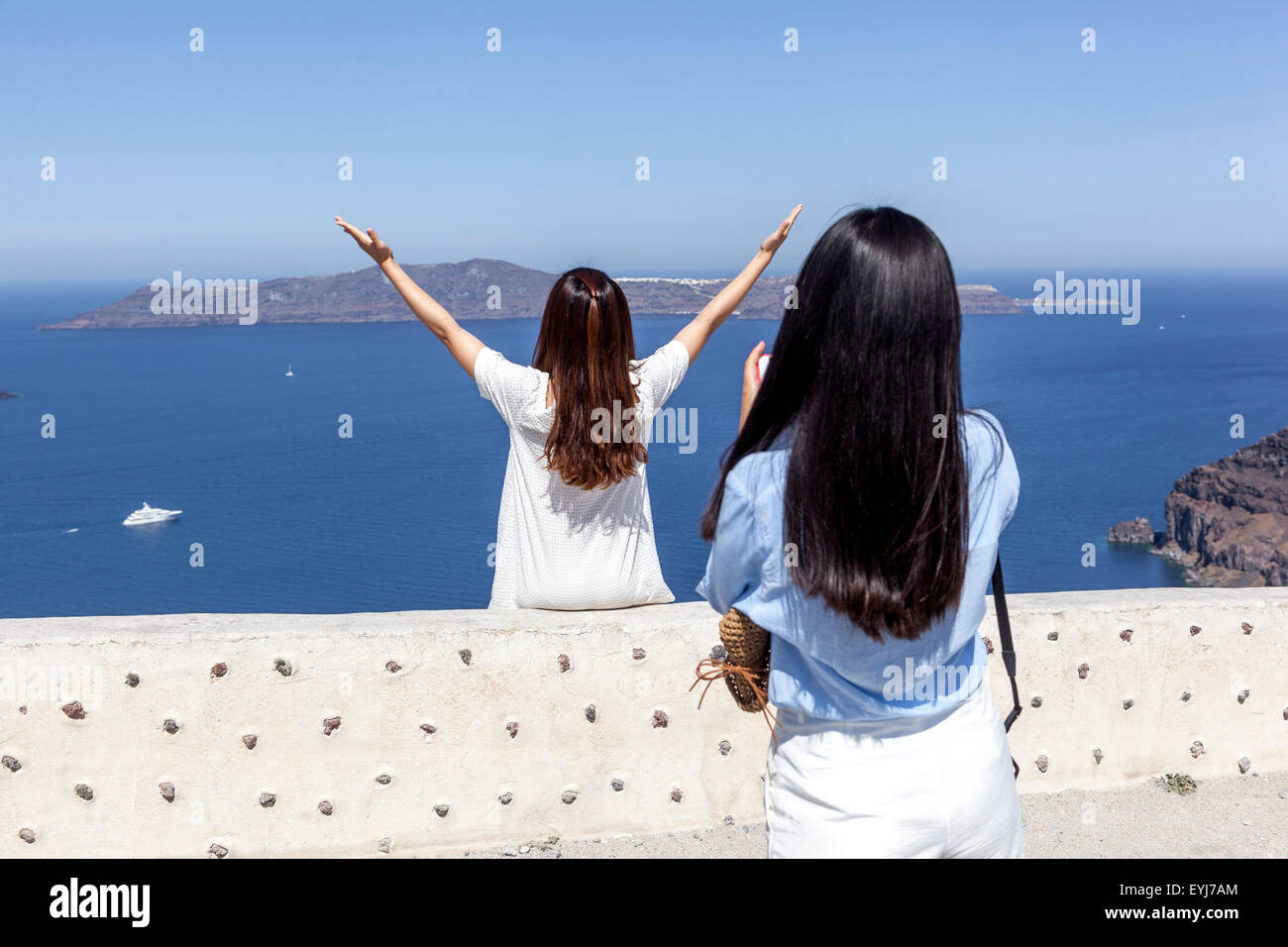 Two young Asian women Europe Greece Santorini, Greek Islands, Cyclades Asian woman raising hands up over the sea Stock Photo
