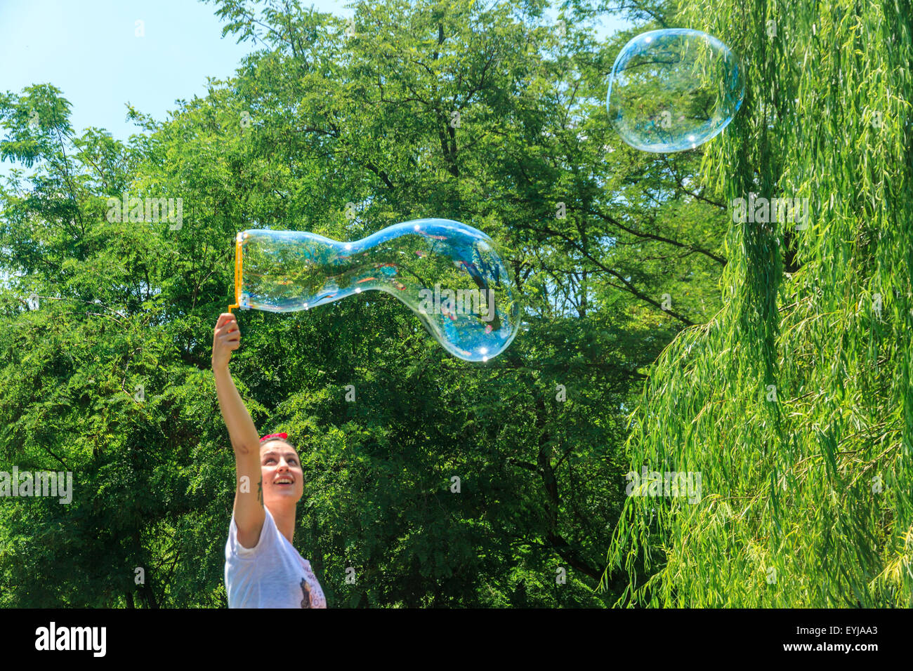 Happy young girl has fun with bubbles in a summer day in a park. She is ...