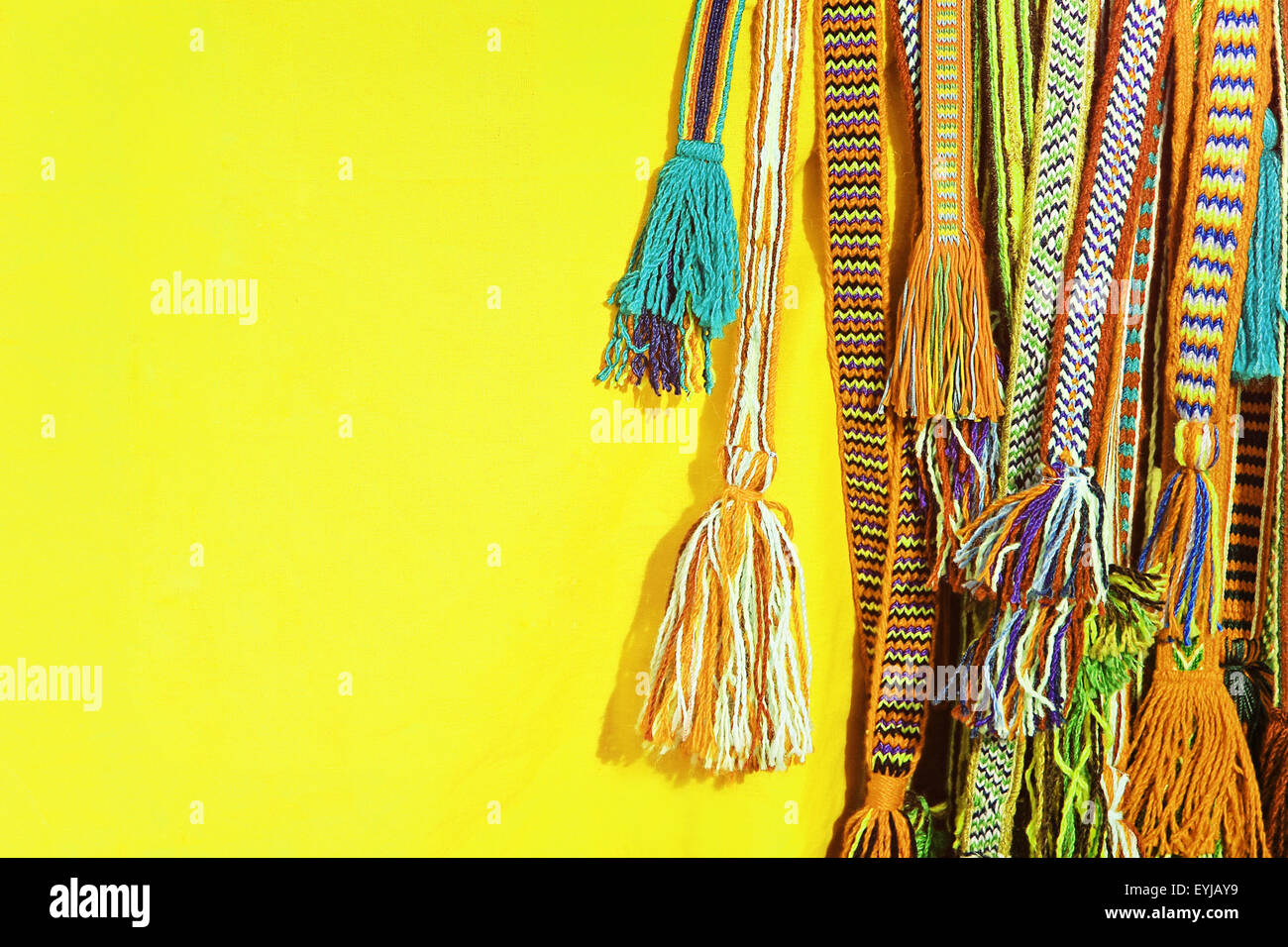 Multicolored tassels of a hippie belts on yellow background. Stock Photo